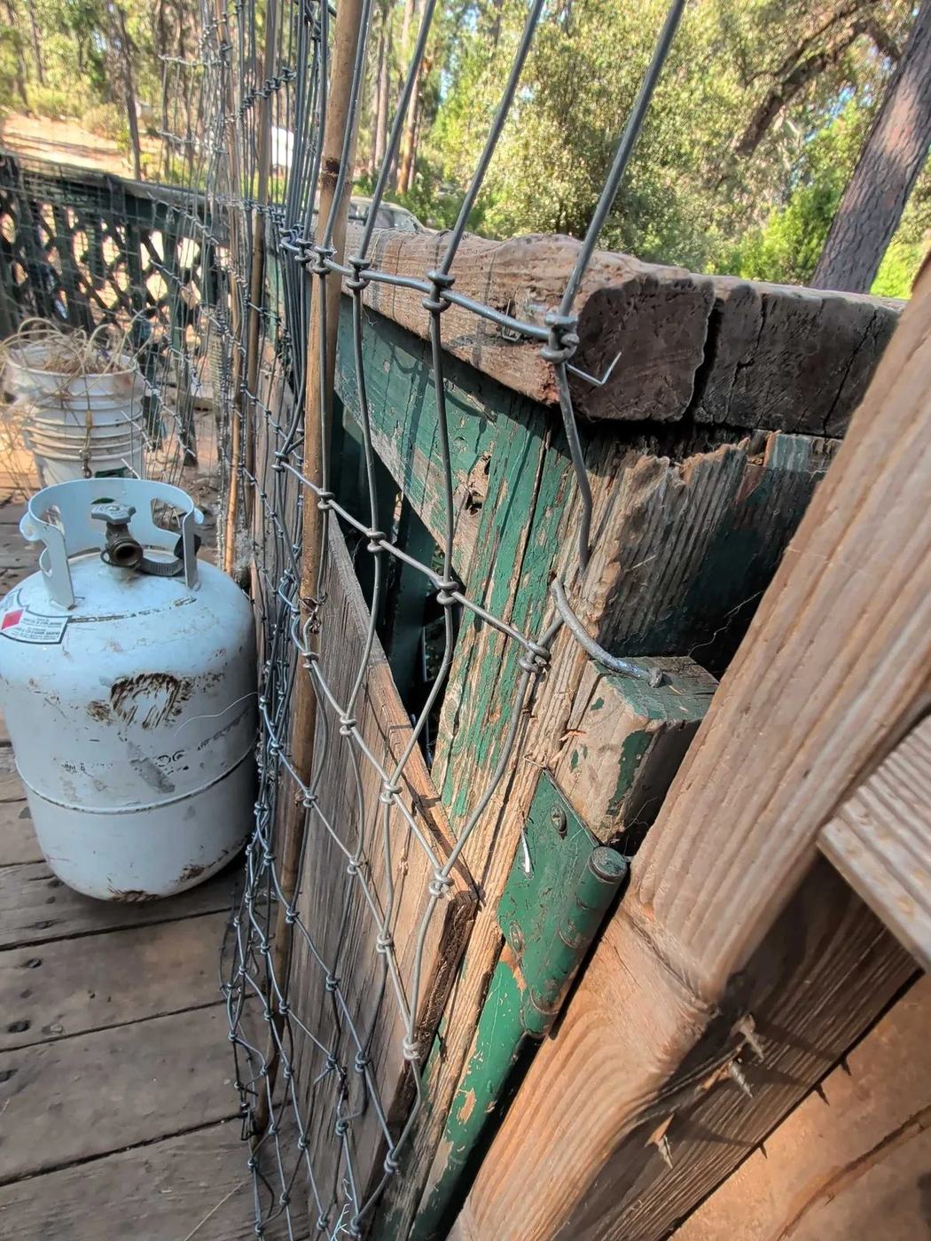 Stacked timber and clutter beside a propane tank